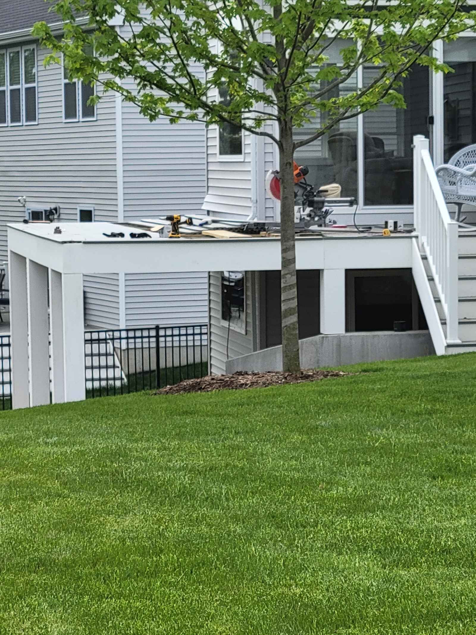 White-framed deck addition under construction behind a gray-sided house, tools and miter saw on the platform