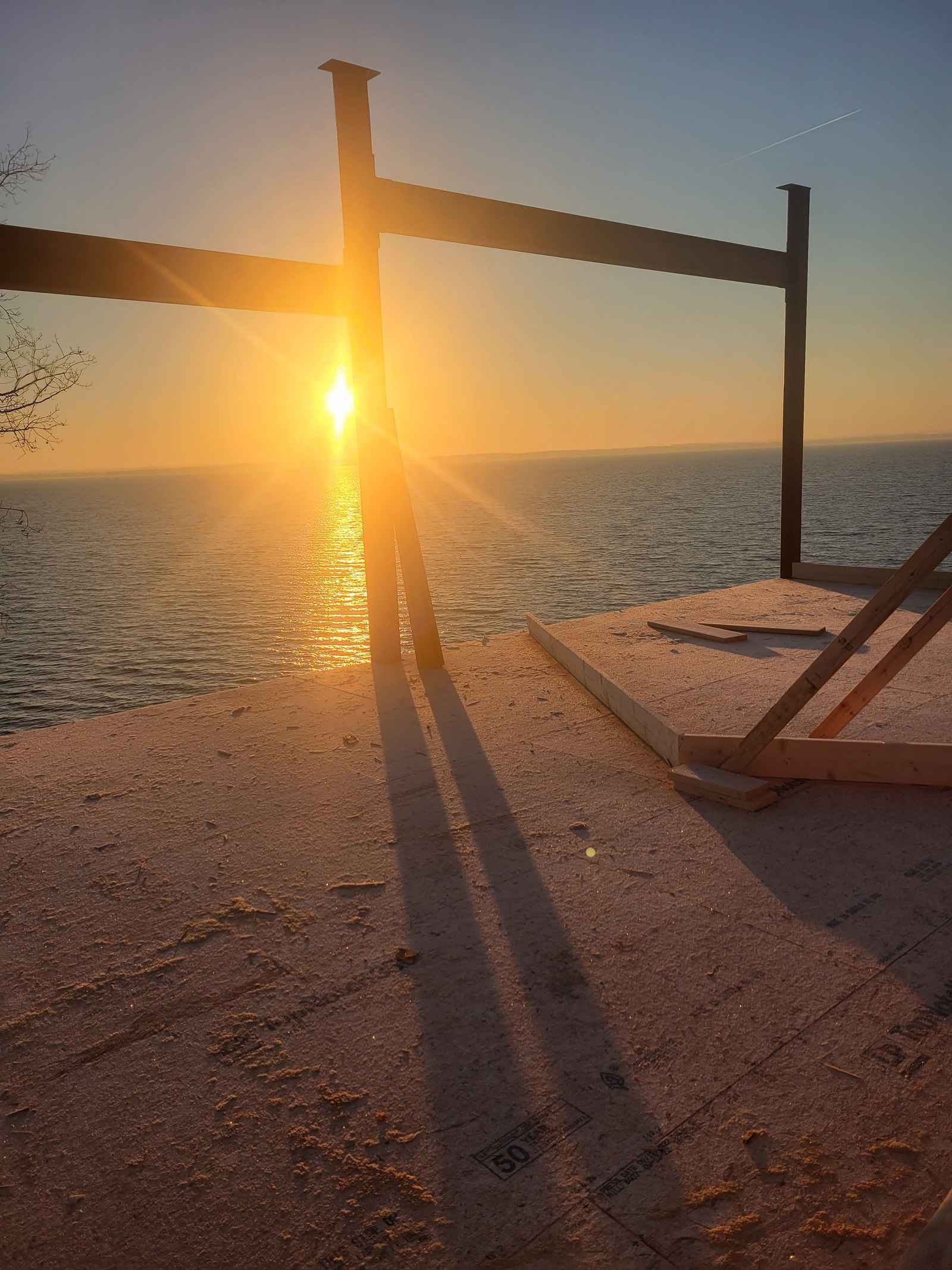 Sunset over open water seen through the steel and wood posts of a lakefront home under construction
